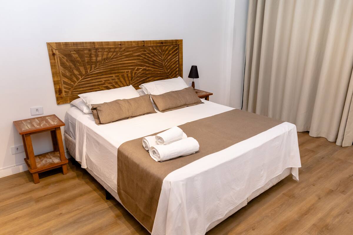 A neatly made bed with a wooden headboard, a small wooden nightstand, and a lamp.