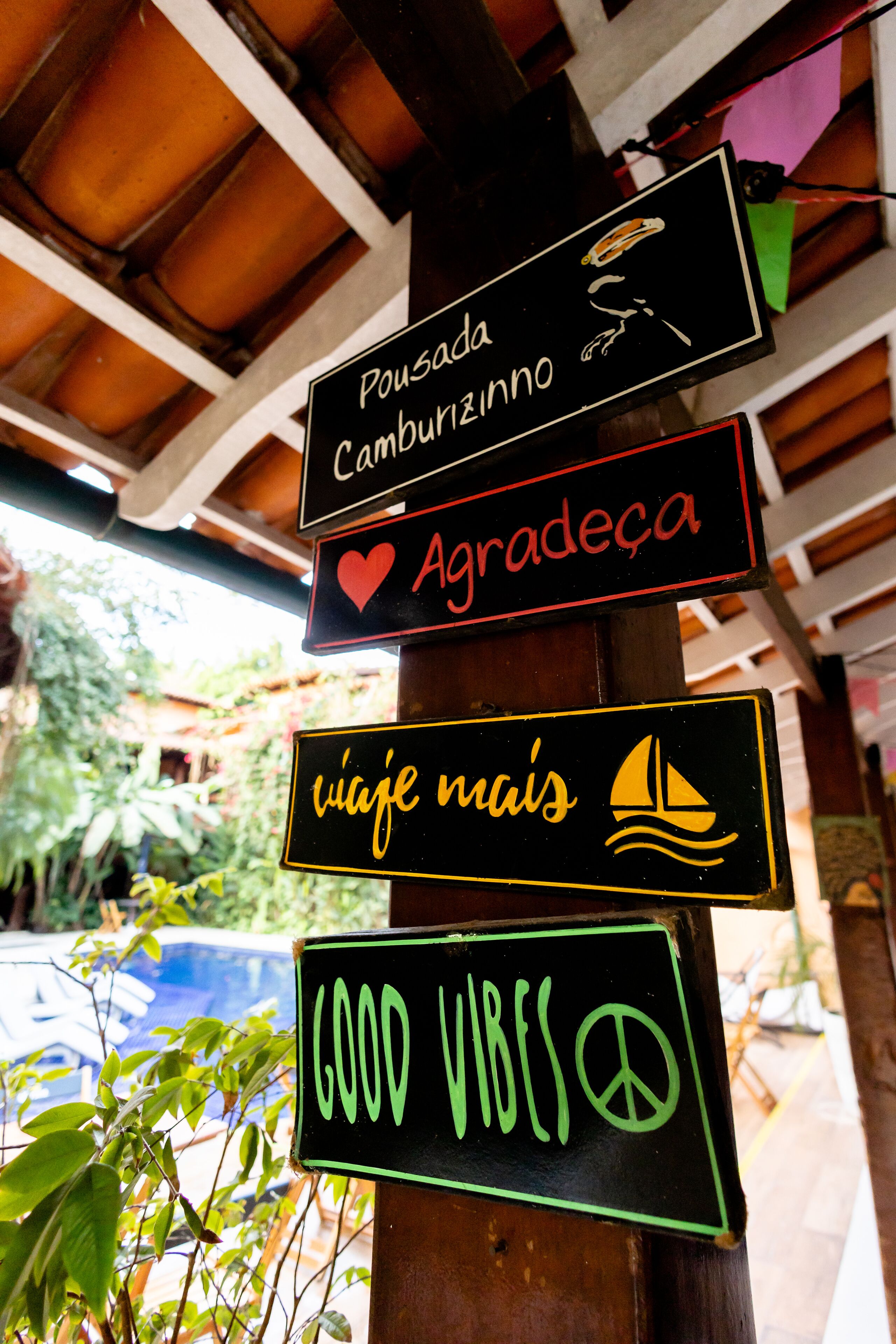 Un letrero con varios mensajes, incluyendo 'Pousada Cambuzinho', 'Agradece', 'viaje más' y 'BUENAS VIBRACIONES'.
