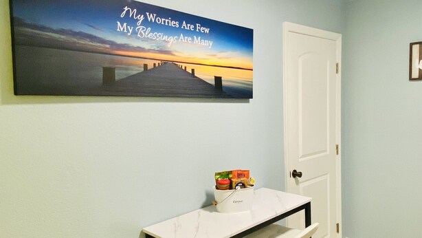 Un couloir avec une porte blanche, une console surmontée d’un plateau en marbre et dotée d’un piétement blanc, et une affiche motivante accrochée au mur.