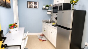 A compact kitchen with a stainless steel refrigerator, white cabinets, a marble countertop, and a welcome sign on the wall.