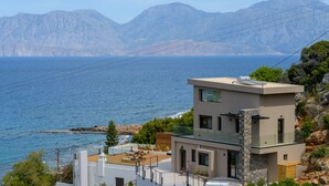 A modern building with a rooftop terrace overlooking a coastal area with mountains in the background. - Beachfront villa with hot tub- breathtaking seaview (Agios Nikolaos)