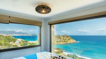 Enjoy a panoramic view of the coastline from the large window in this hotel room, featuring a neatly made bed and a convenient breakfast tray.
