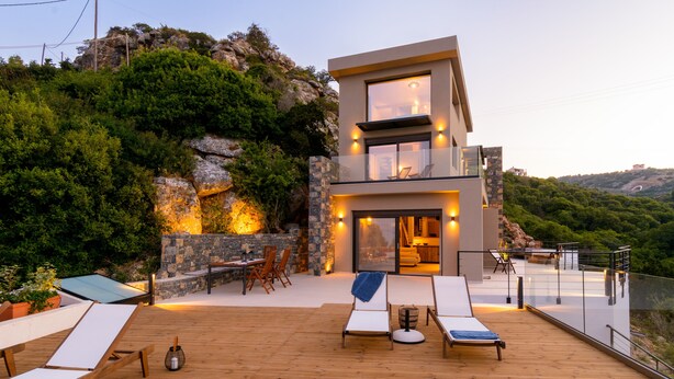 A modern two-story house with a wooden deck, outdoor seating, and a stone wall. - Beachfront villa with hot tub- breathtaking seaview (Agios Nikolaos)