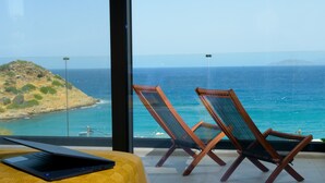 A balcony with two wooden lounge chairs and a laptop on a yellow ottoman, overlooking a coastal view with a clear sky. - Beachfront villa with hot tub- breathtaking seaview (Agios Nikolaos)