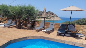 A pool area with lounge chairs and umbrellas, overlooking a rocky coastline. - Beachfront villa with hot tub- breathtaking seaview (Agios Nikolaos)