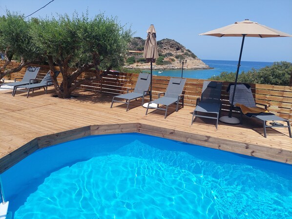 Zona de piscina con sillas de descanso y sombrillas, con vistas a un litoral rocoso.