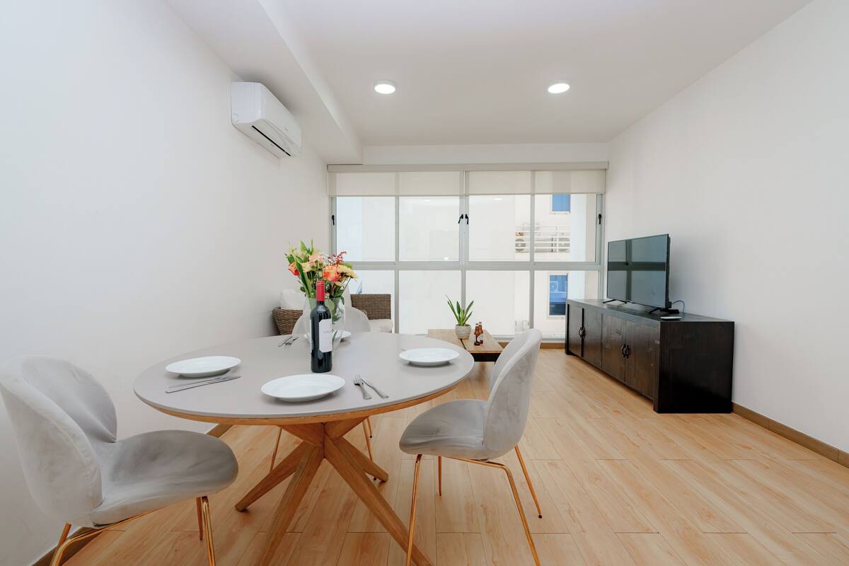 A modern dining area with a round table, four chairs, a wine bottle, and a vase of flowers.