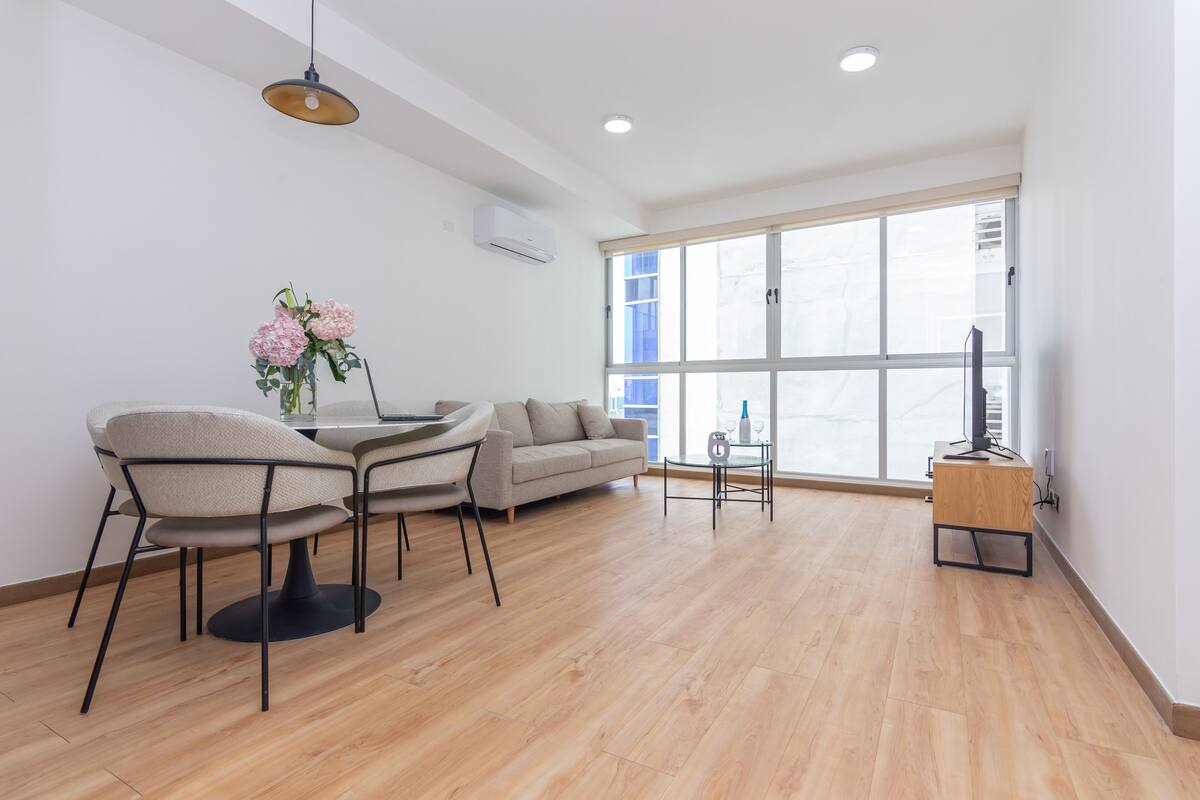A modern living room with a round table, two chairs, a sofa, and a TV stand.