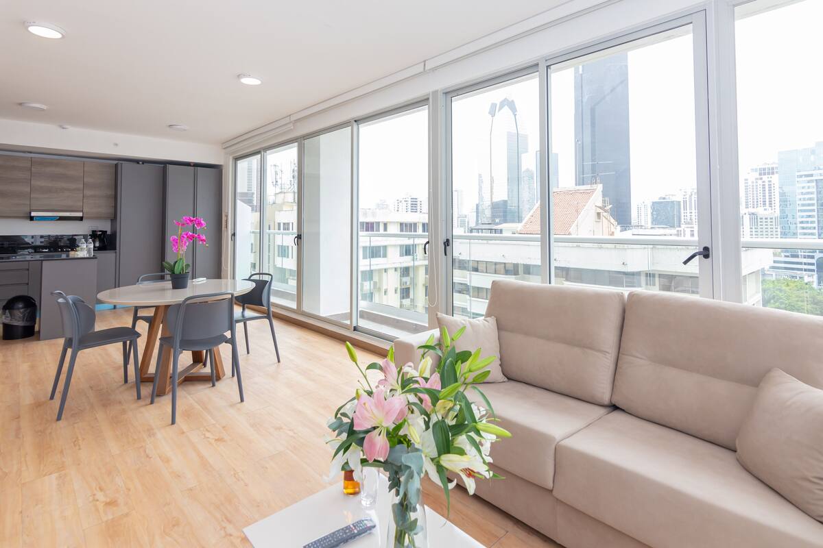 A modern living room with a sofa, dining table, chairs, and a vase of flowers.