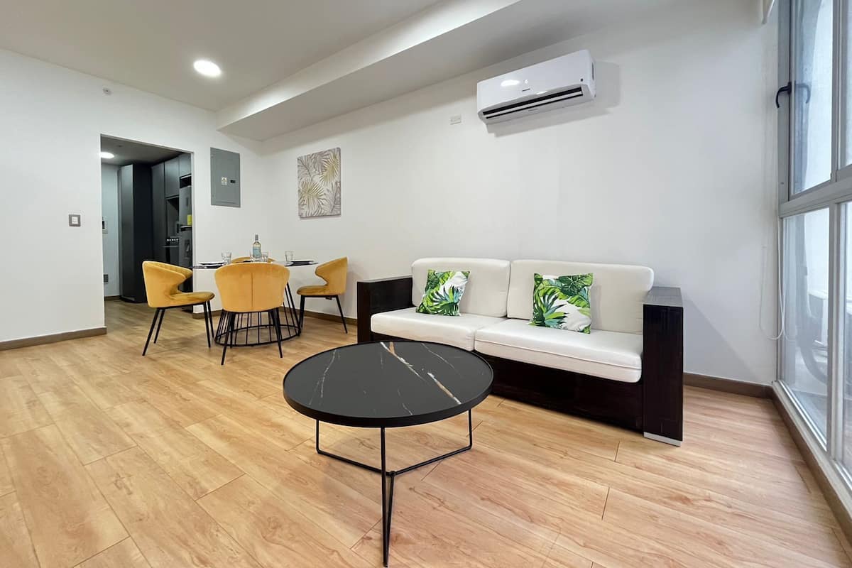 A modern living room with a sofa, a round coffee table, and a dining area with chairs and a table.