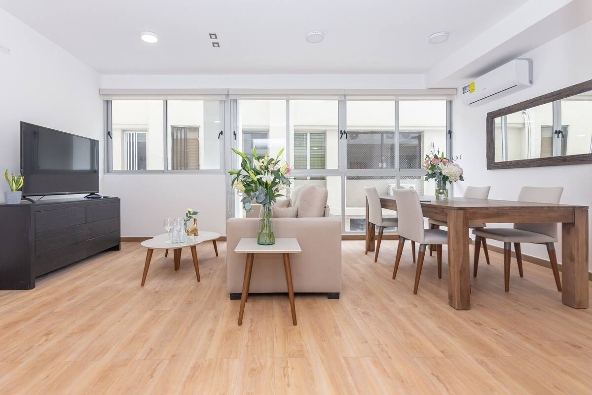 A modern living room with a sofa, coffee table, TV, and dining area.