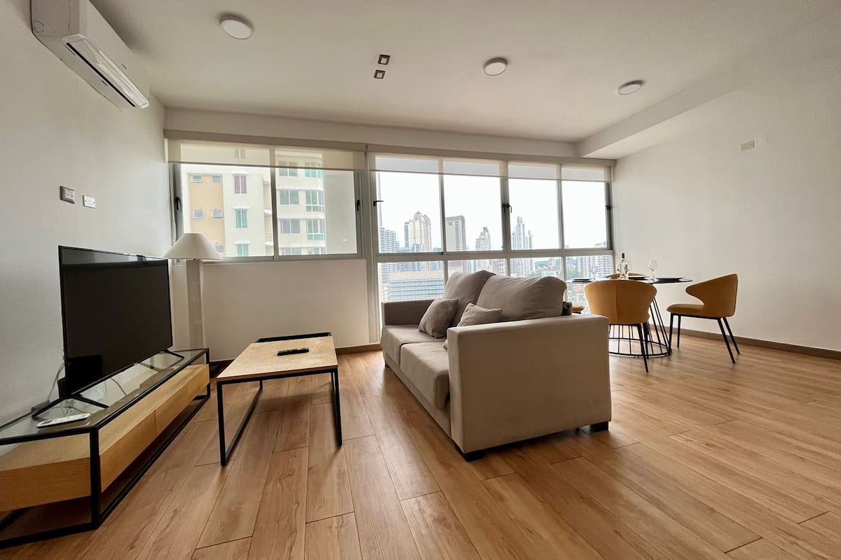 A modern living room with a sofa, TV, and dining area.