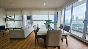 Een moderne woonkamer met een eettafel, stoelen, een bank en een groot raam met uitzicht op de stad.