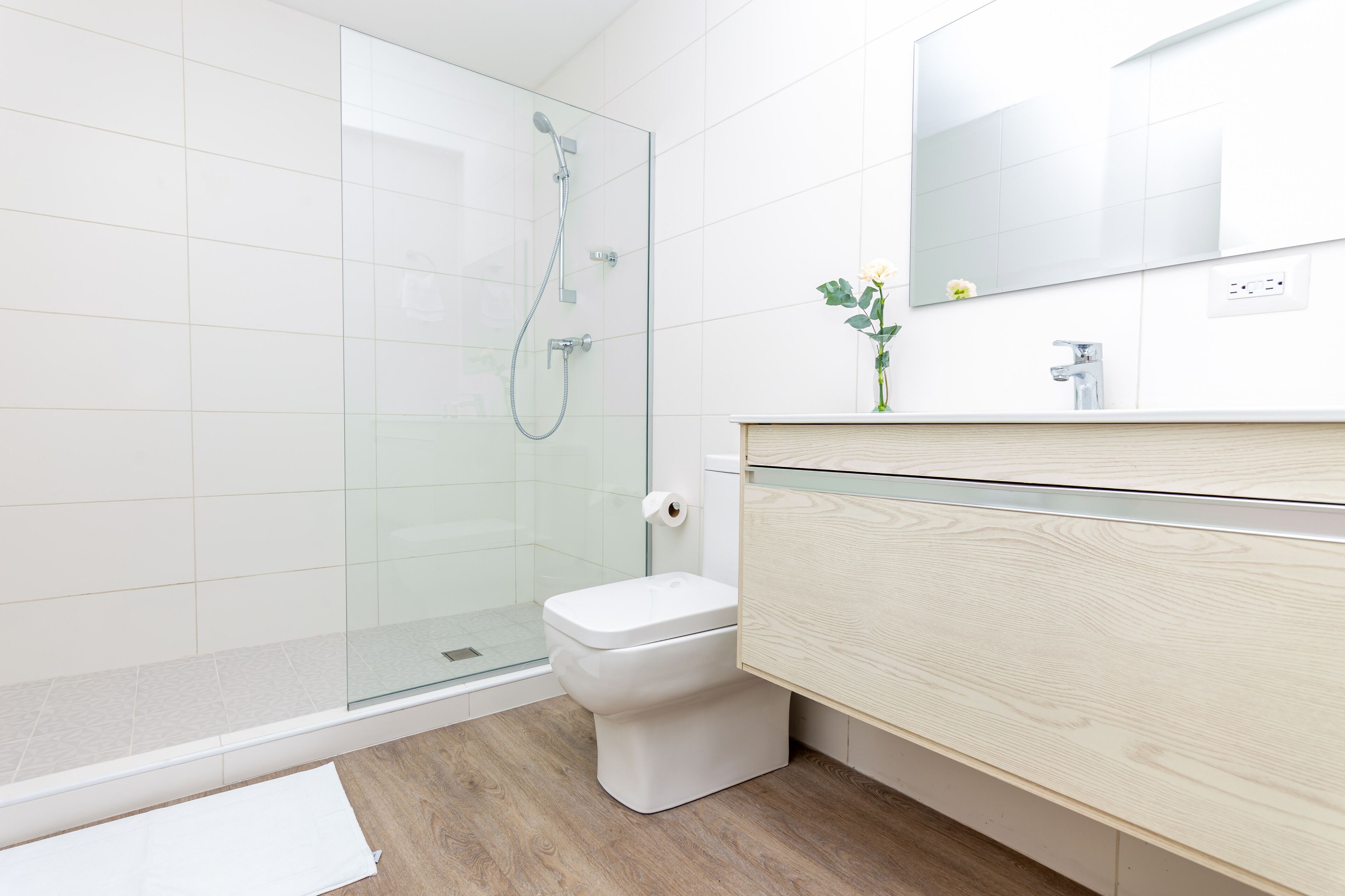 A modern bathroom with a glass shower enclosure, a white toilet, and a wooden vanity with a mirror.