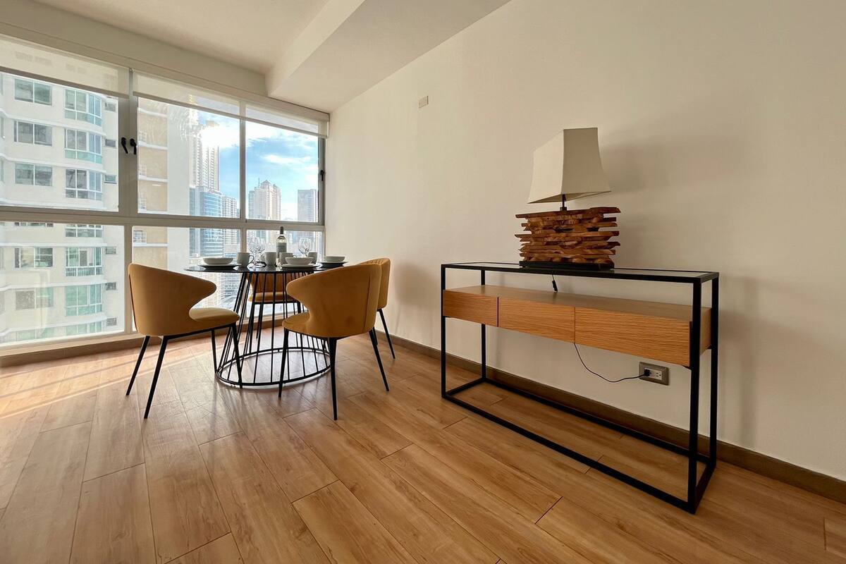 A modern living room with a dining area, large windows, and a view of the cityscape.