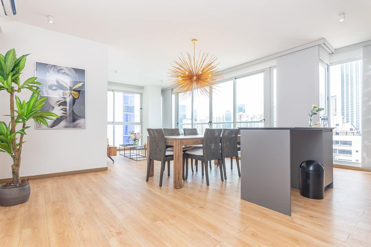 A modern dining area with a wooden table and chairs, a potted plant, and a city view through large windows.