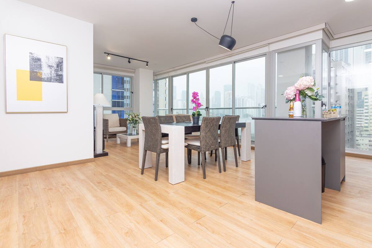A modern kitchen with a dining area, large windows, and a city view.