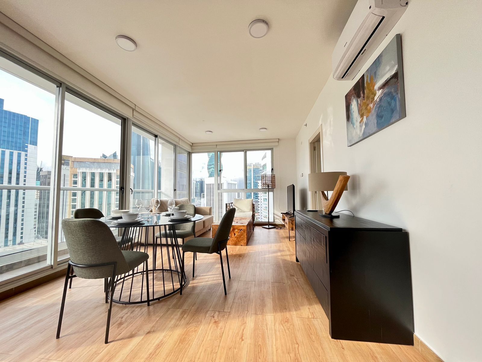 Una sala moderna con comedor, ventanas amplias y vista a la ciudad.