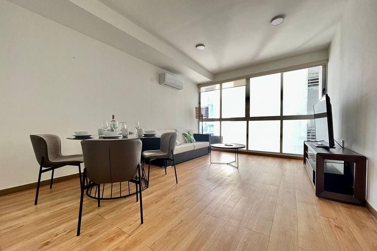 A modern living room with a dining area, large windows, and a flat-screen TV.