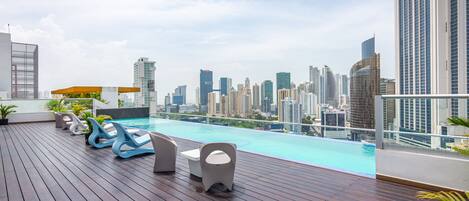 Zona de piscina en la azotea con sillones de descanso y vista al horizonte de la ciudad.