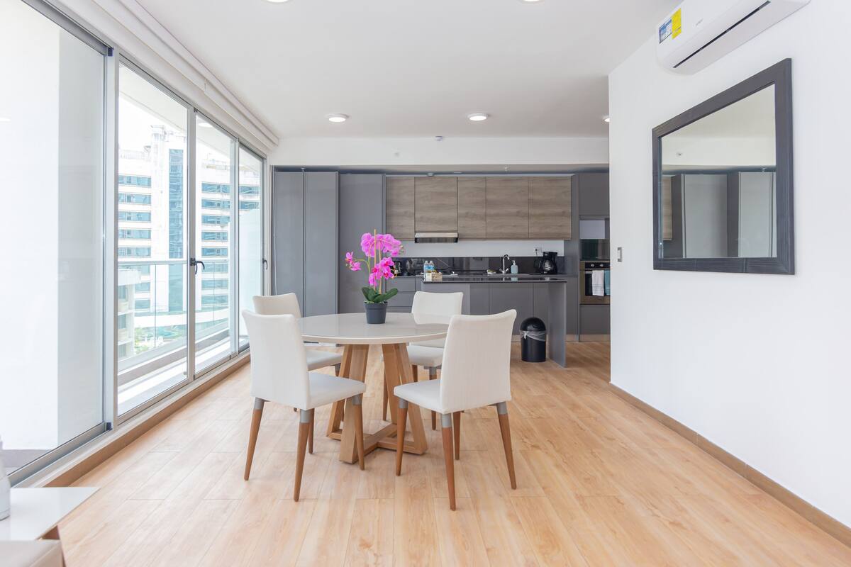 A modern kitchen with grey cabinets, a central island, and a dining area with a round table and white chairs.