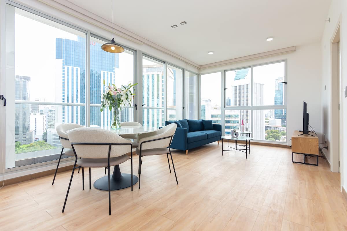 A modern living room with a dining area, large windows, and a view of city buildings.