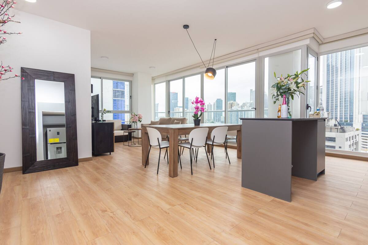 A modern kitchen with a dining area, large windows, and a city view.