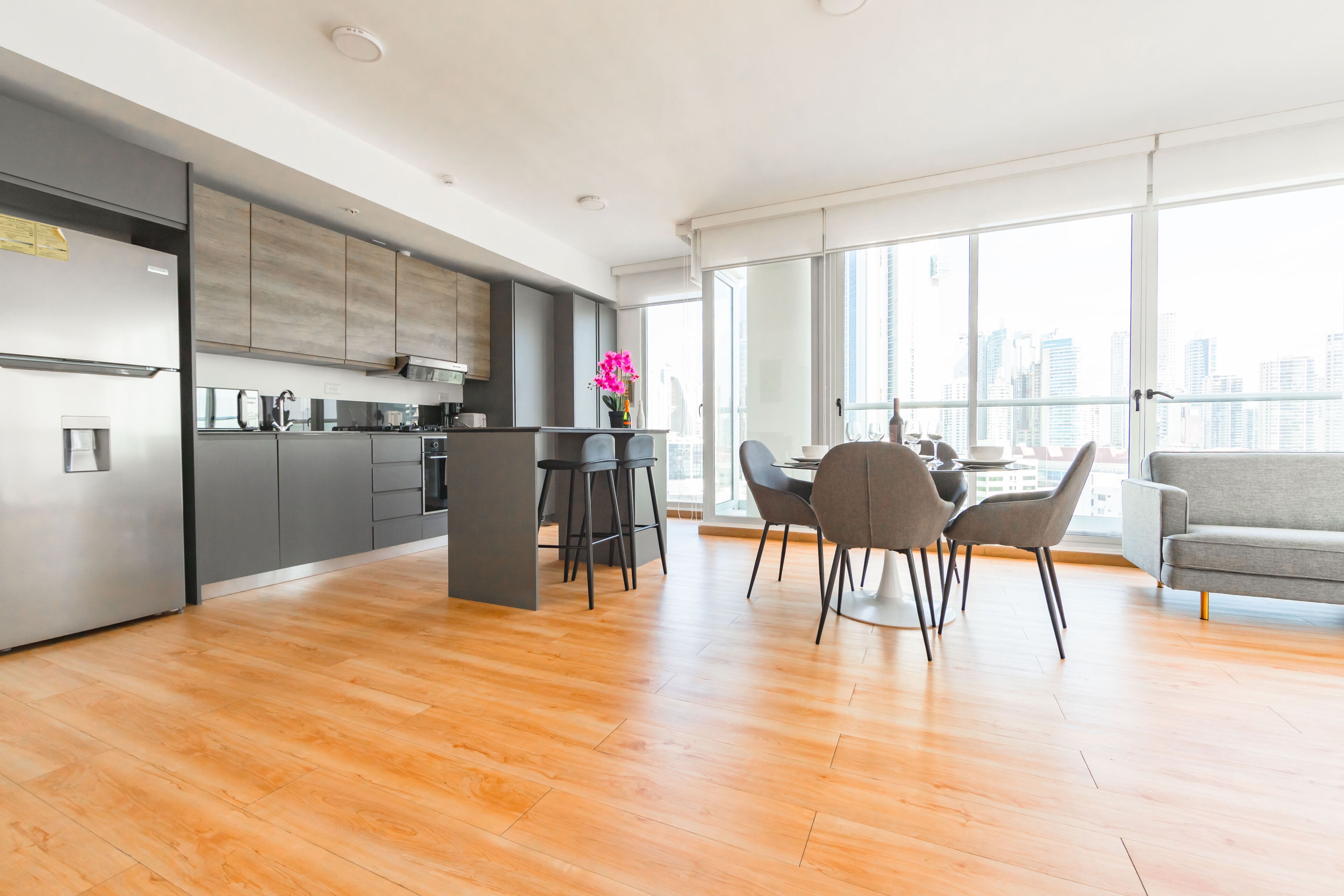 A modern kitchen with grey cabinets, a central island, and a dining area with a grey sofa and chairs.