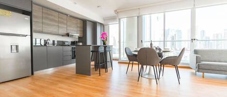 A modern kitchen with grey cabinets, a central island, and a dining area with a grey sofa and chairs.