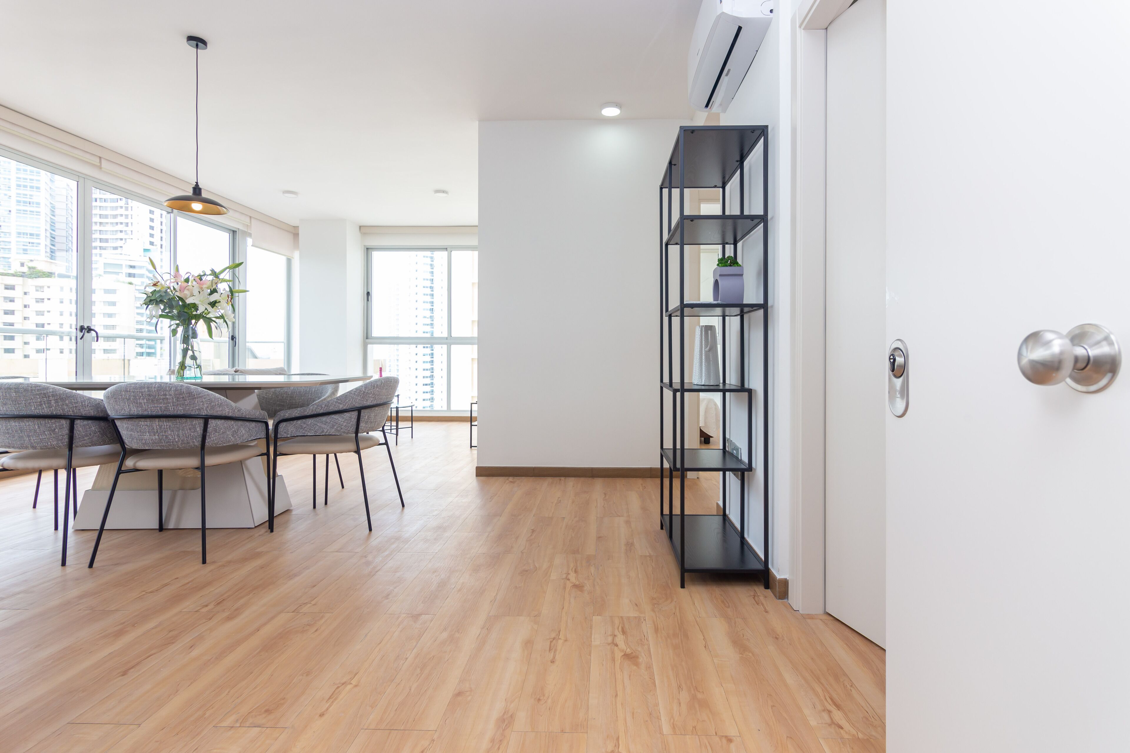Una cocina moderna con comedor, suelo de madera, estantería empotrada y amplios ventanales con vistas a la ciudad.