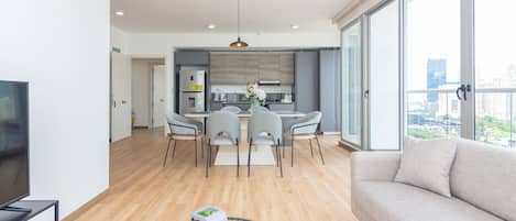 A modern apartment with a dining area, kitchen, and a large window offering a city view.