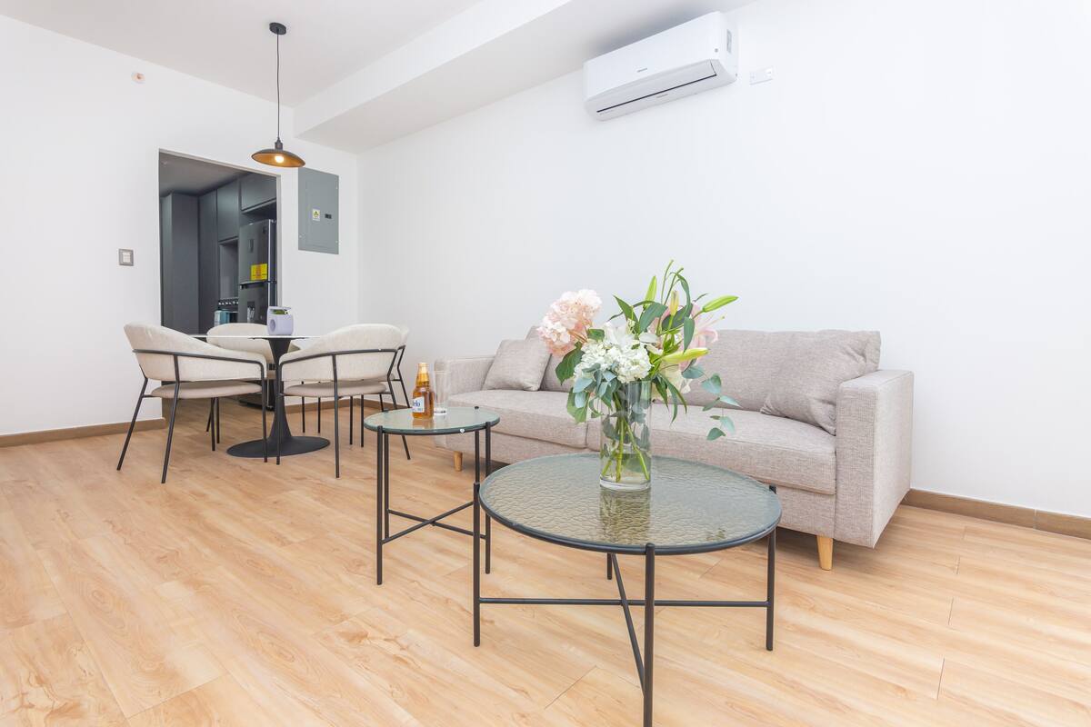 A modern living room with a sofa, two round tables, and a dining area with chairs.