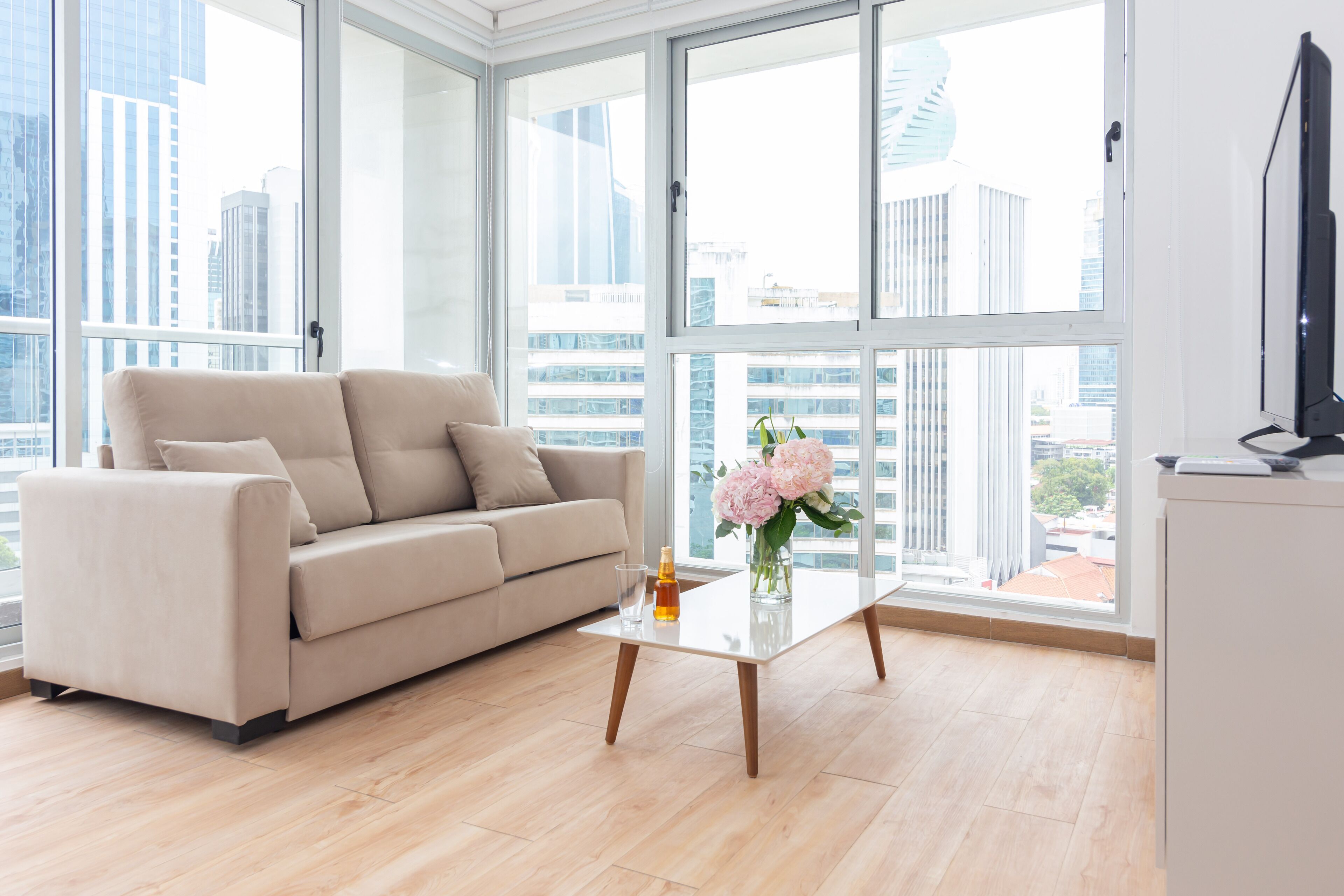 A modern living room with a beige sofa, a glass coffee table, and a vase of flowers.