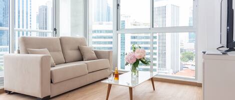 A modern living room with a beige sofa, a glass coffee table, and a vase of flowers.