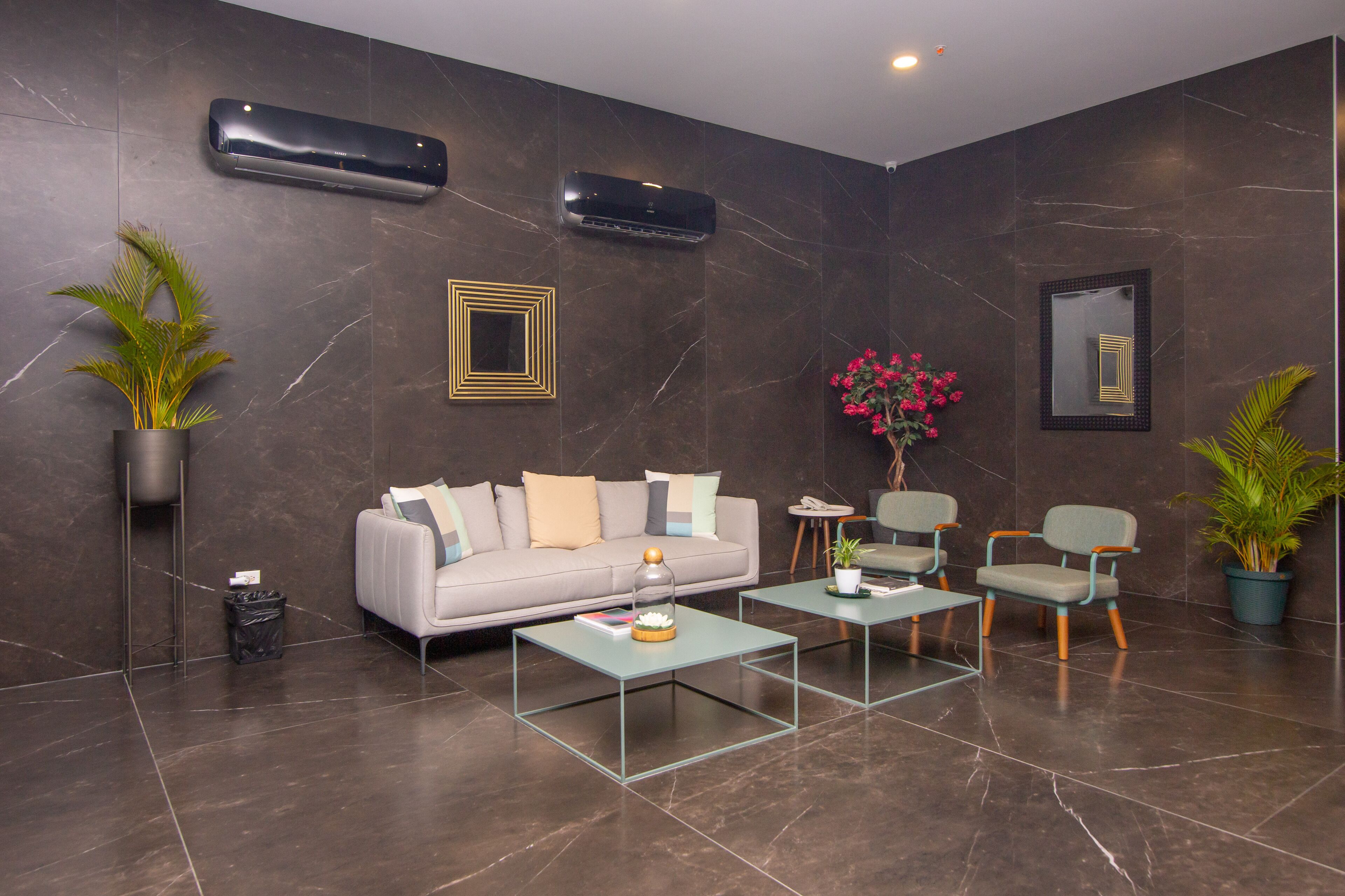 A modern lobby with a sofa, two armchairs, a coffee table, and decorative plants.