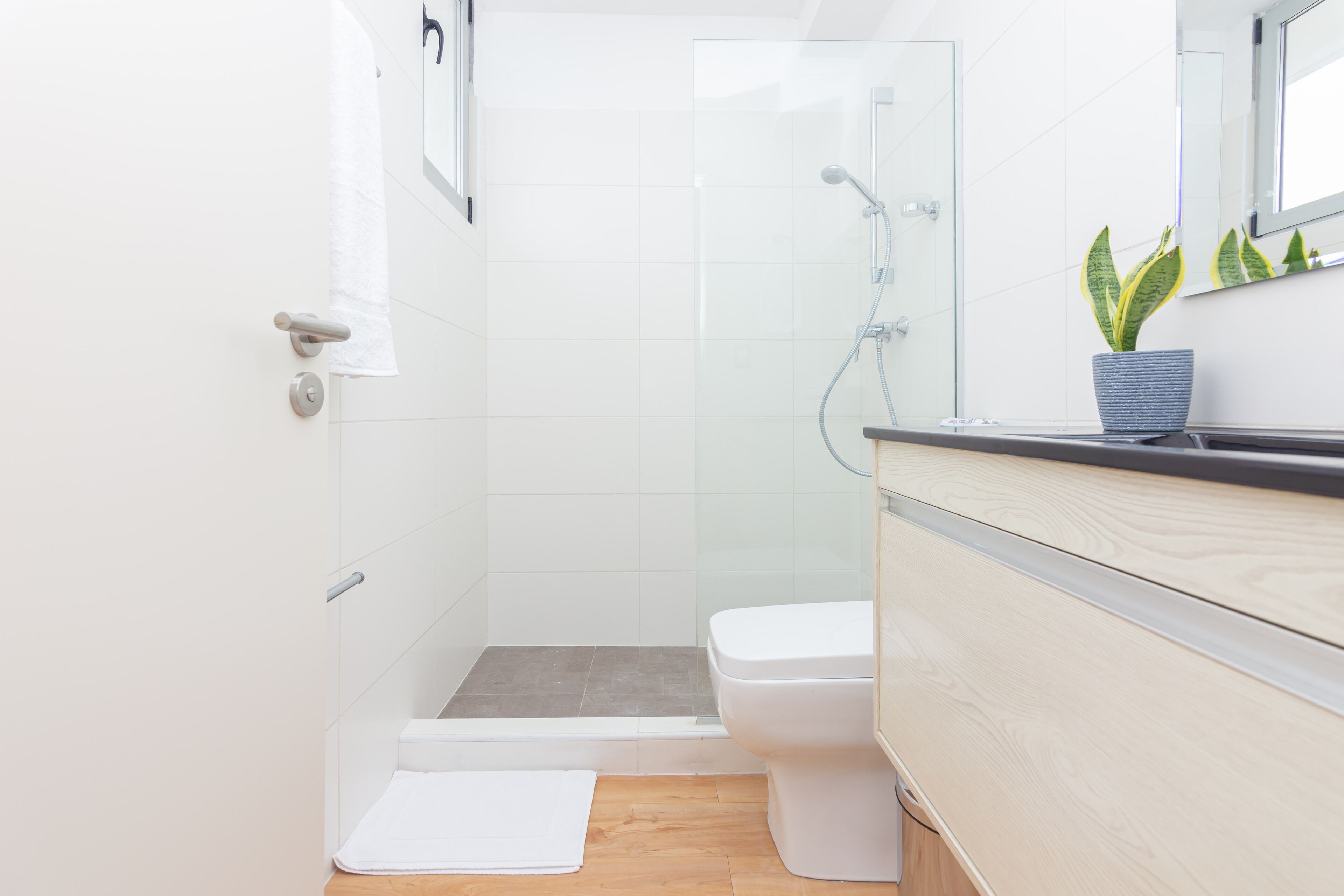 Une salle de bain moderne avec une douche à parois de verre, des toilettes blanches et un meuble-lavabo en bois avec un miroir.