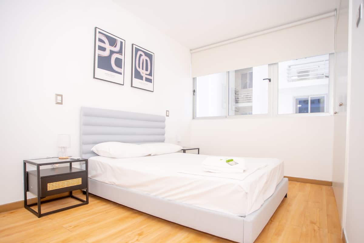 A modern bedroom with a bed, a nightstand, a window, and two wall art pieces.