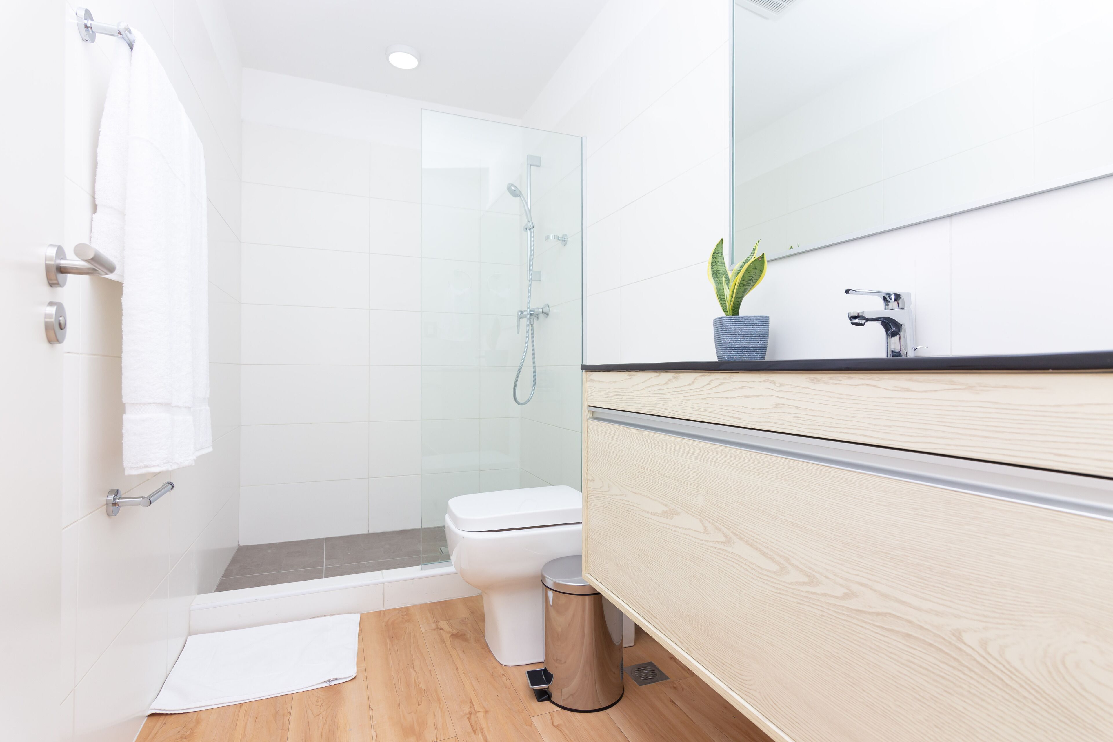 A modern bathroom with a glass-enclosed shower, a white toilet, and a wooden vanity with a mirror.