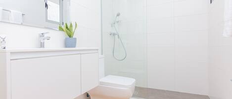 A modern bathroom with a glass-enclosed shower, a white toilet, and a sink with a mirror above it.