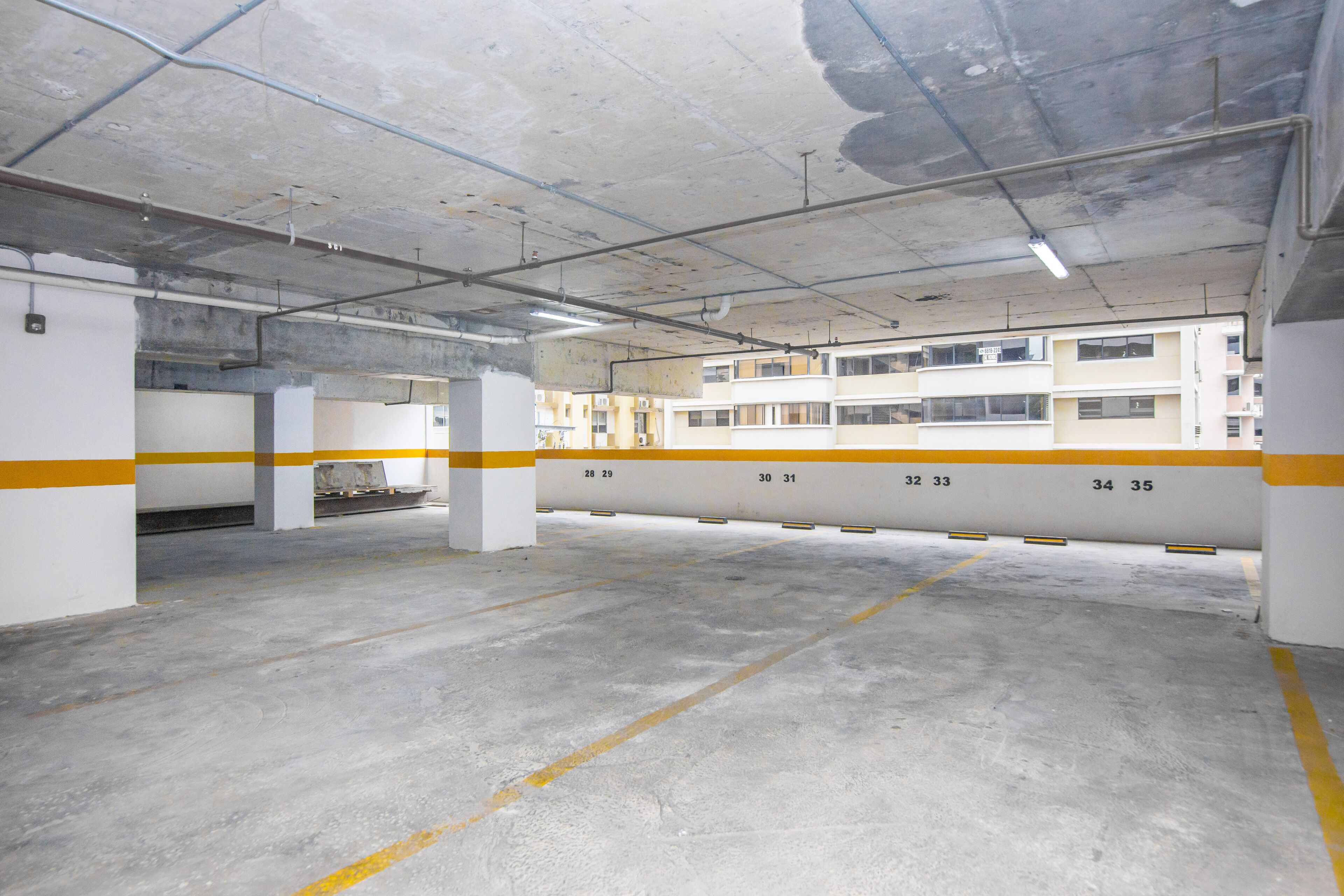 Eine Tiefgarage mit Betonböden und -säulen, nummerierten Stellplätzen und sichtbaren Bauelementen wie Rohren und Leuchten.