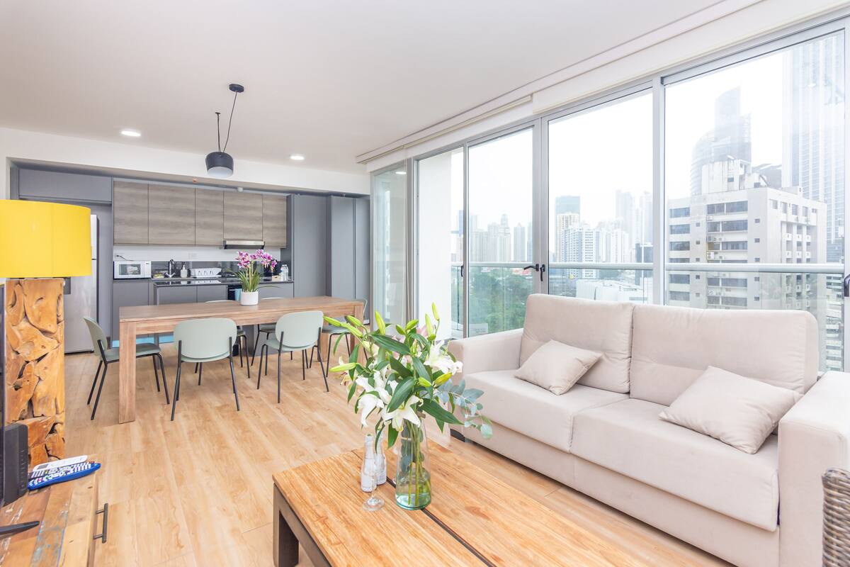 A modern living room with a sofa, coffee table, and a dining area with chairs and a table.
