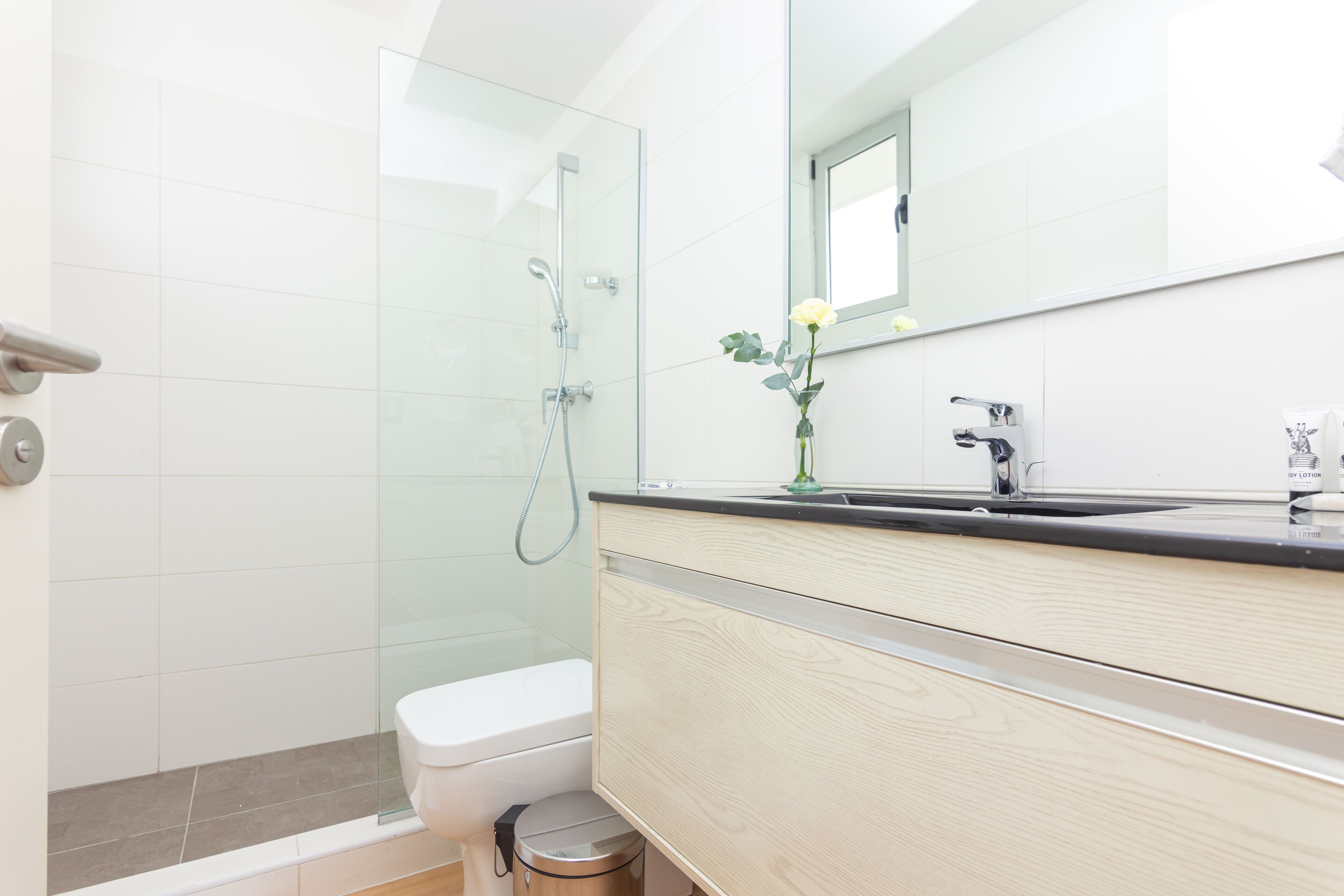 Un baño moderno con cabina de ducha de vidrio, inodoro, lavabo con espejo y un cubo de basura.