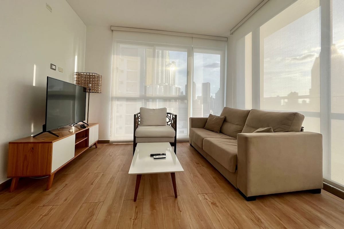 A modern living room with a flat-screen TV, a wooden coffee table, a beige sofa, and a chair.