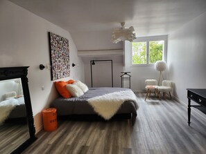 Un dormitorio moderno con una cama grande, un espejo, un cuadro abstracto colorido, una lámpara de pie y vistas a zonas verdes por la ventana.