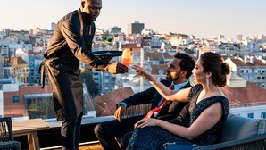 A rooftop bar with a city view, a bartender serving drinks, and guests seated on a couch. - Hills Hotel Lisboa (Lisbon)