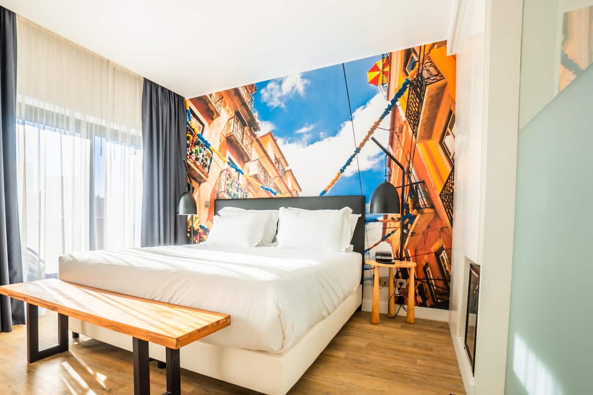 A modern hotel room with a large bed, a bench, a desk, and a mural of a cityscape.