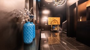 A modern hotel lobby with a dark floor, a blue vase with branches, a gold cart, and a wall-mounted light fixture. - Hills Hotel Lisboa (Lisbon)