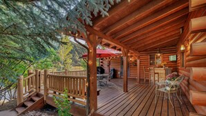 Une terrasse en bois avec des meubles d’extérieur, un espace abrité agrémenté d’un parasol rouge, et une vue sur le paysage environnant.