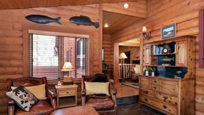 L’intérieur chaleureux d’un chalet en rondins, avec des fauteuils en cuir, un meuble en bois orné d’objets décoratifs et un poisson suspendu au plafond.