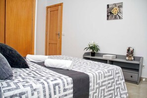 Une chambre à coucher avec un lit, une porte en bois, une console grise et un tableau accroché au mur.